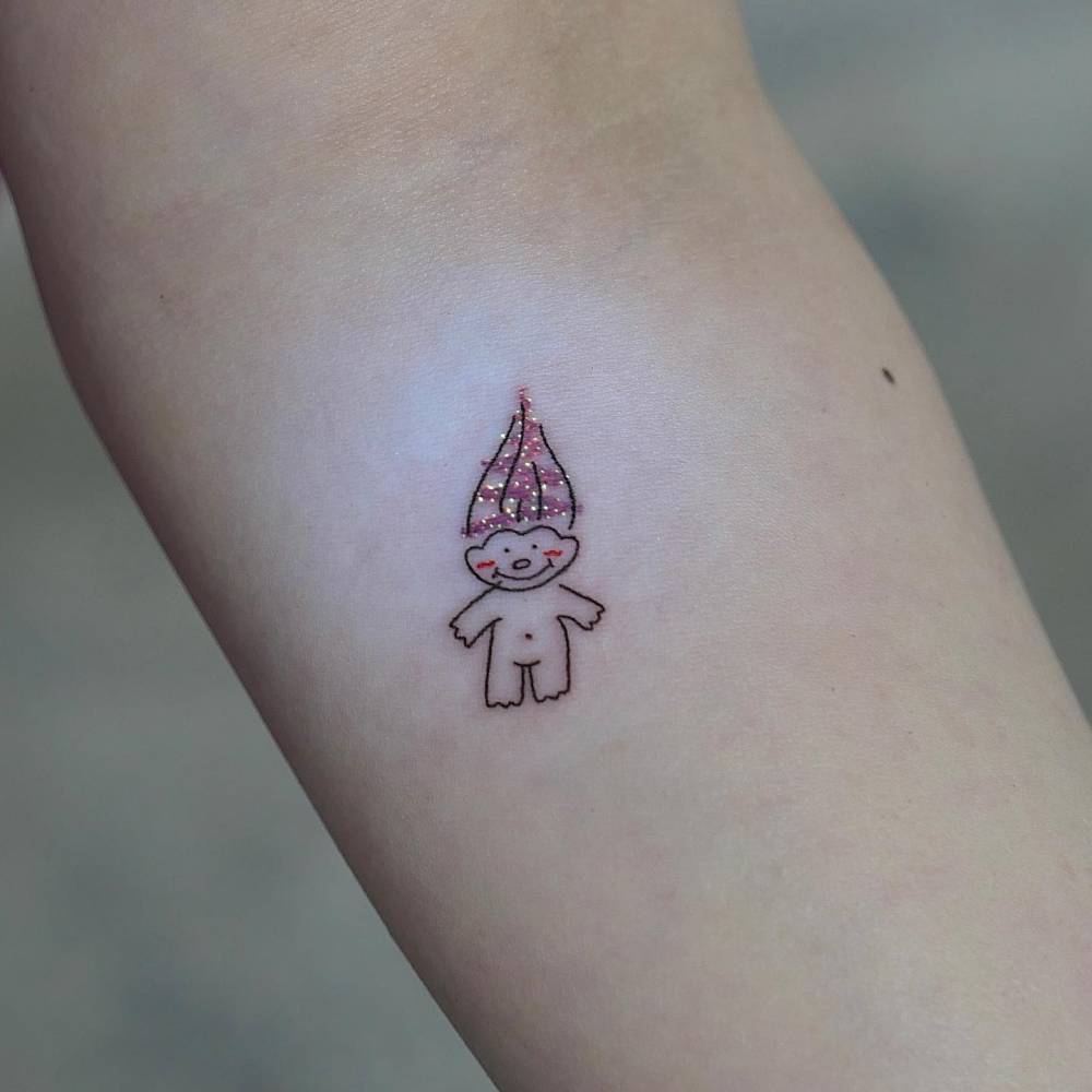 Cartoony style Troll doll tattoo located on the inner forearm.