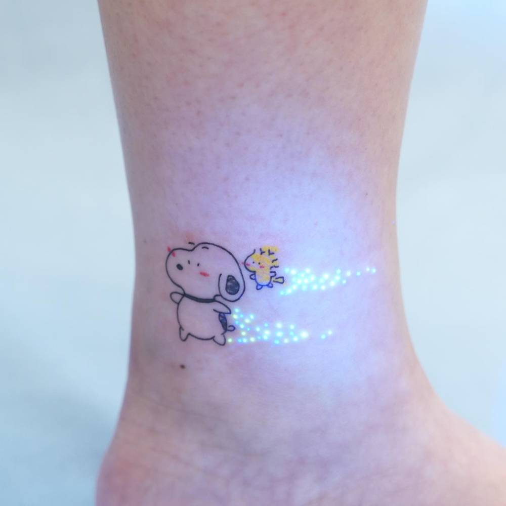 Snoopy and Woodstock in cartoon style tattooed on the ankle.