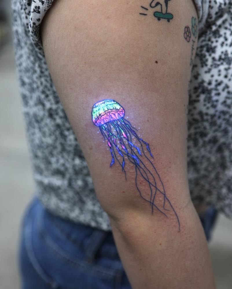 UV ink jellyfish tattoo located on the upper arm, illustrative style.