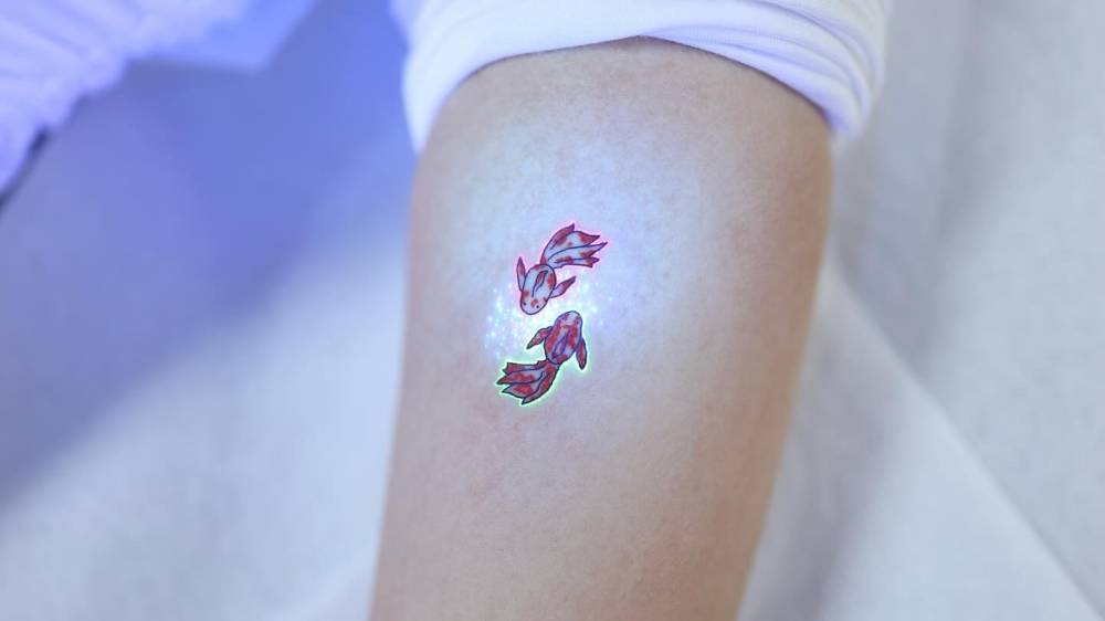 Cartoon style two opposite fish tattoo located on the inner forearm.