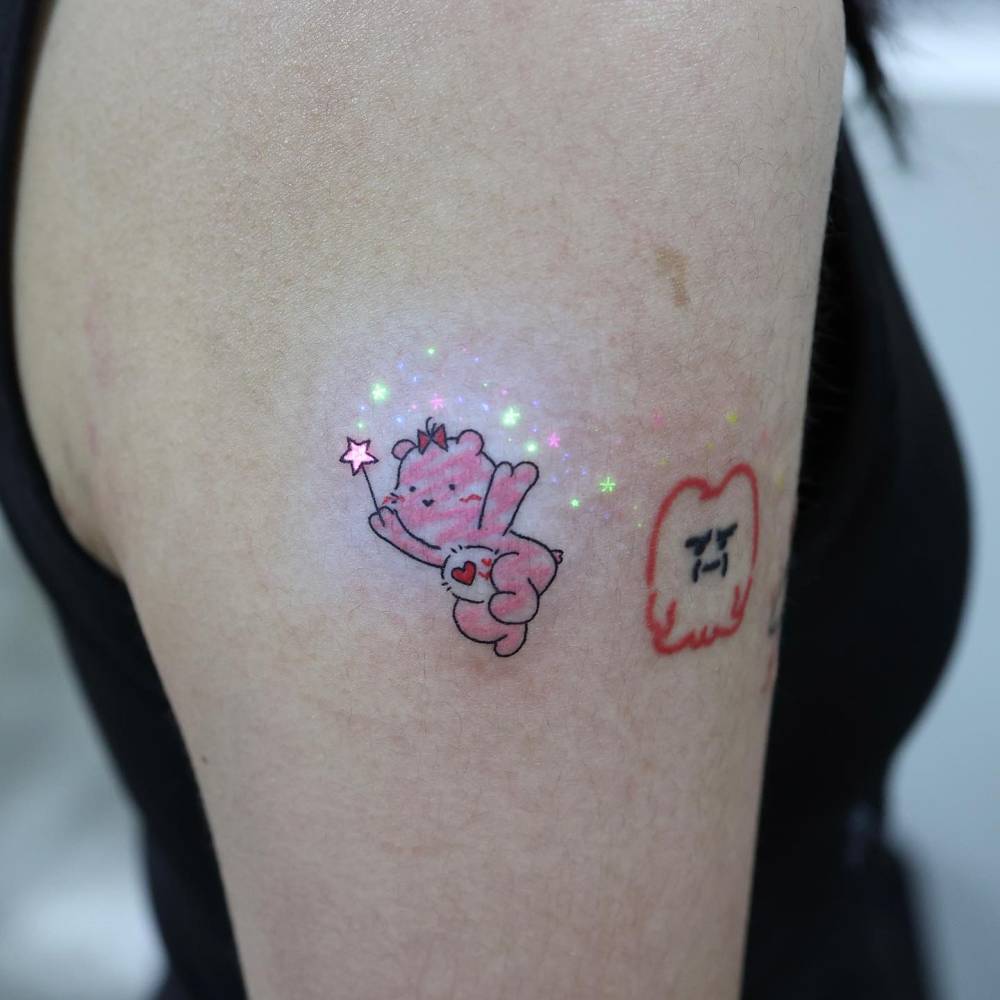 Care Bear tattoo in cartoon style located on the upper arm.