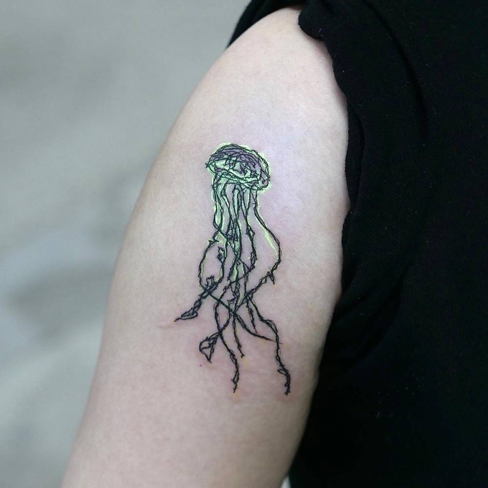 Illustrative style UV ink jellyfish tattooed on the upper arm.