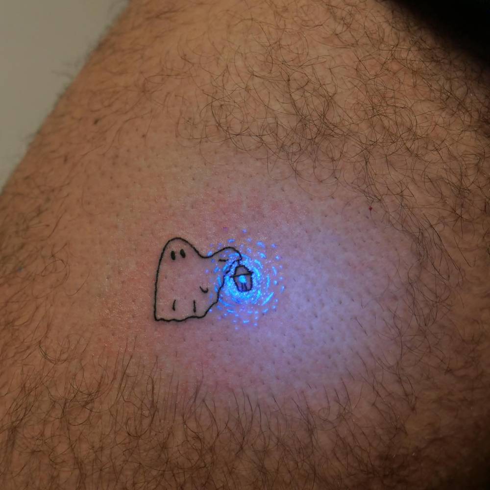 Cartoon style ghost tattoo in UV ink located on the thigh.