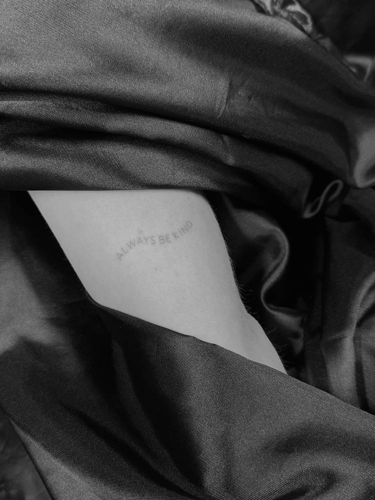 "Always be kind" lettering tattoo located on the upper arm.