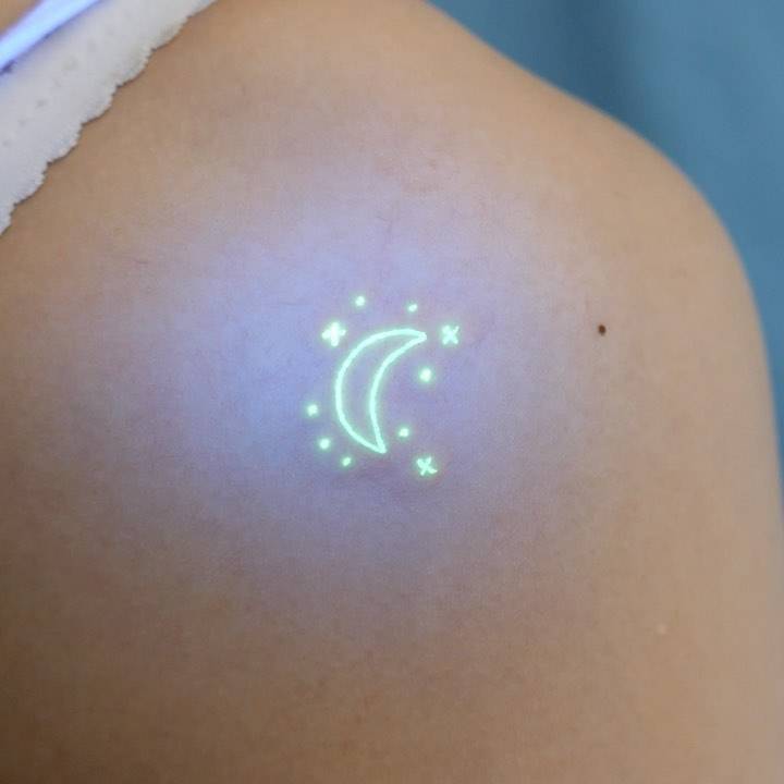 UV ink crescent moon and stars tattoo located on the shoulder blade.