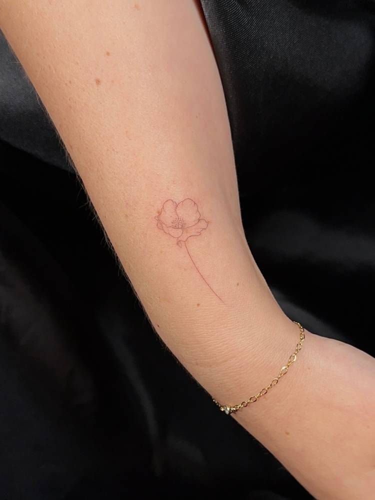 Poppy flower tattoo in fine line style located on the wrist.