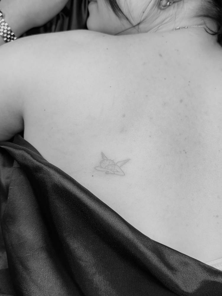 Sleeping cherub tattoo placed on the shoulder blade, done in fine line style.