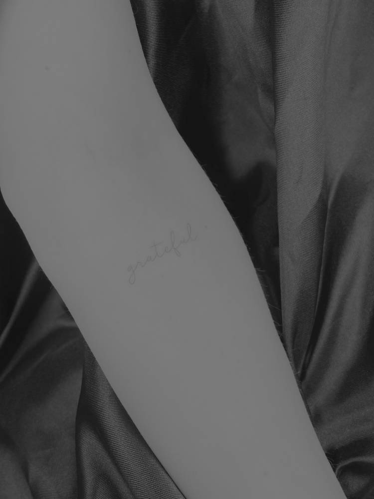 Lettering tattoo of the word "grateful" located on the inner forearm.