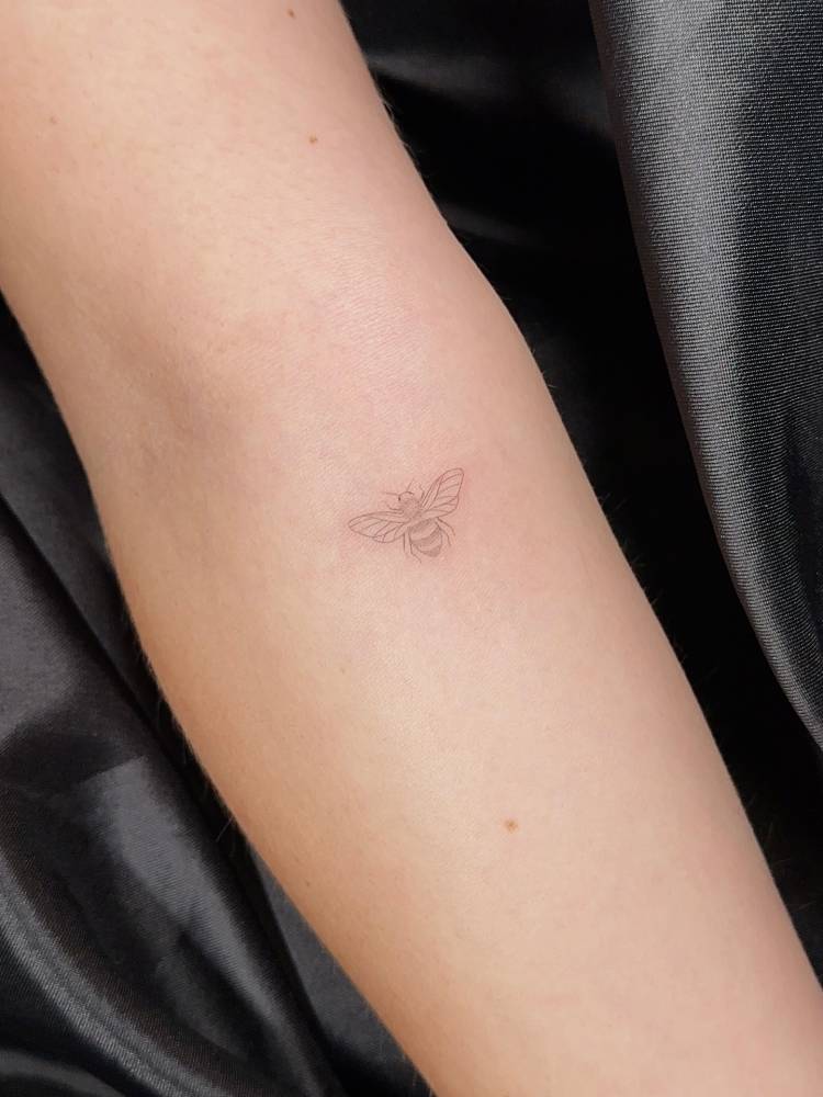 Tiny bee tattoo in fine line style done on the inner forearm.
