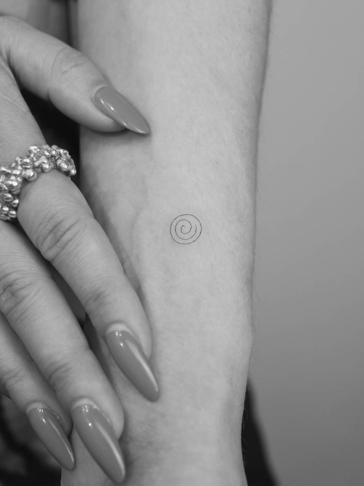 Tiny minimalistic tattoo of a spiral located on the wrist.
