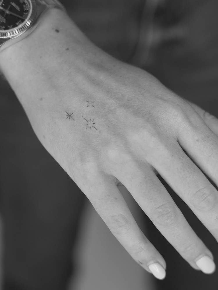 Sparkling stars tattoo in minimalistic style located on the hand.