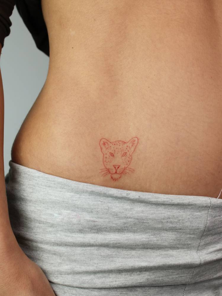 Leopard portrait tattoo in red ink located on the hip.