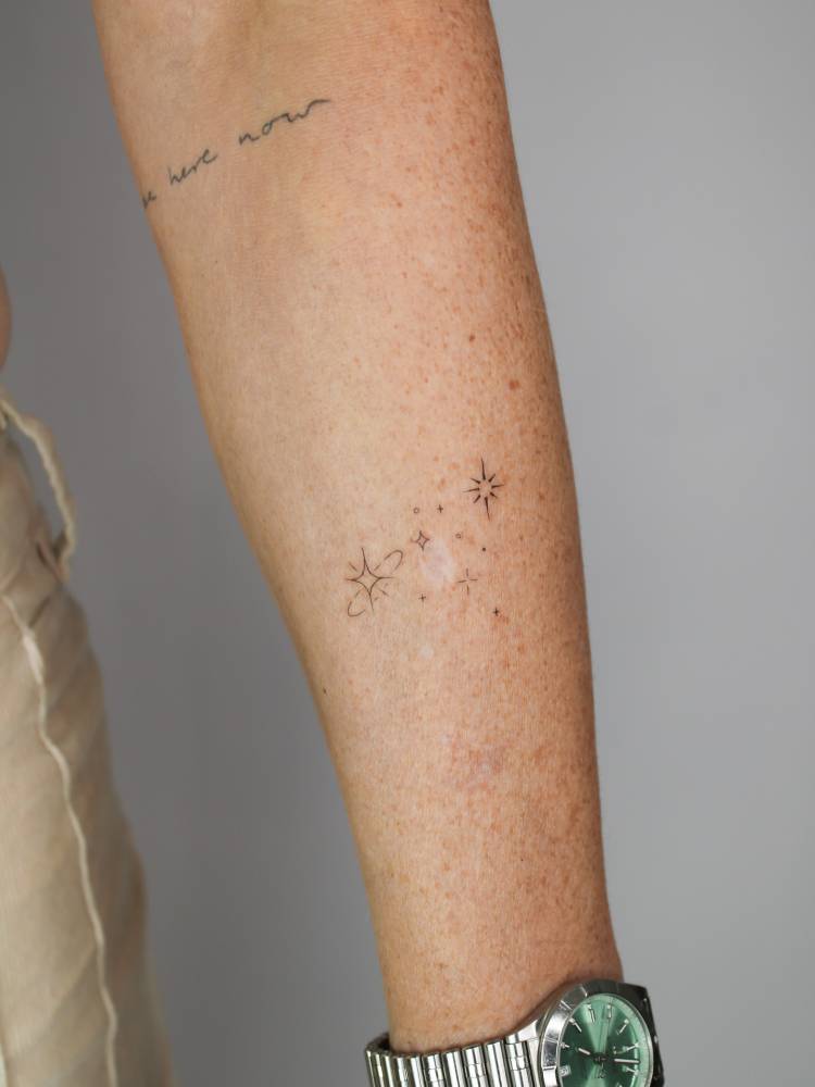 Sparkling stars tattooed on the forearm, done in minimalistic style.