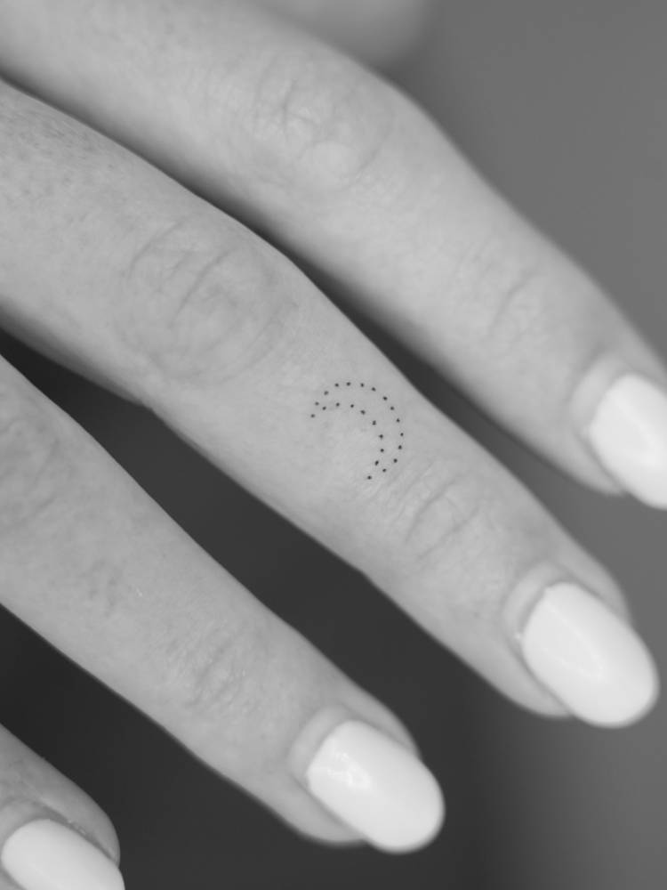Tiny minimalistic dotted crescent moon tattooed on the finger.