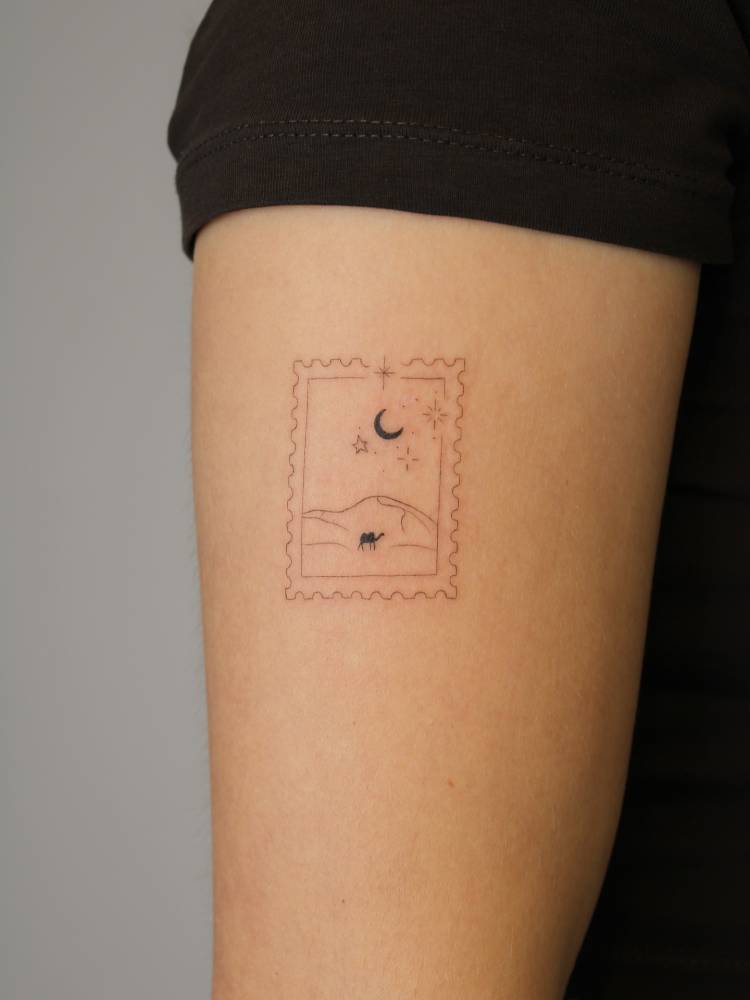 Desert stamp tattoo located on the upper arm, fine line style.