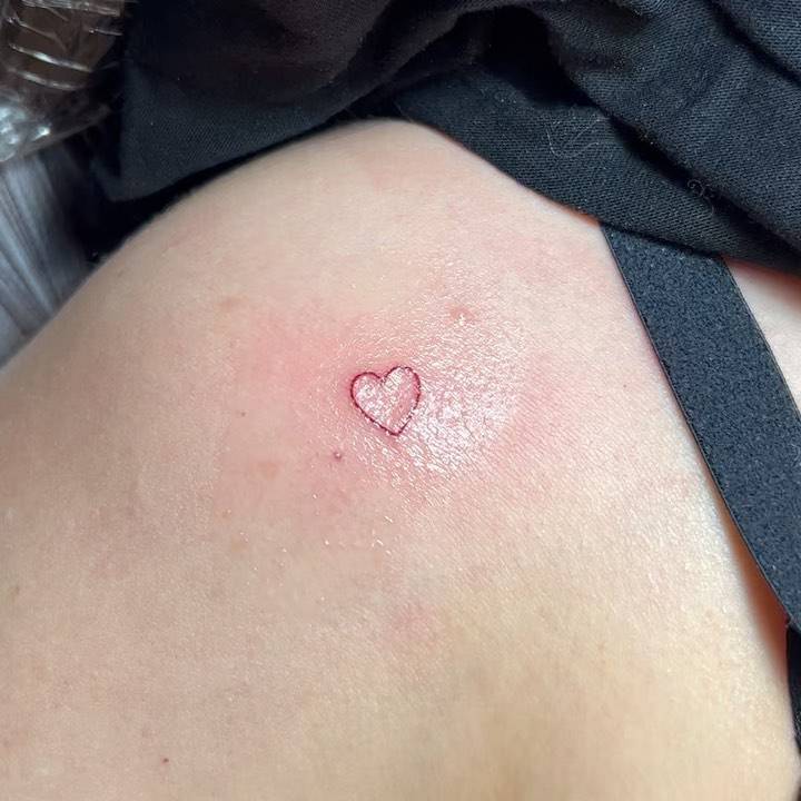 Minimalistic red heart tattoo located on the shoulder.