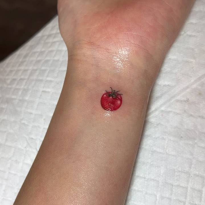 Micro-realistic style tiny tomato tattoo located on the wrist.