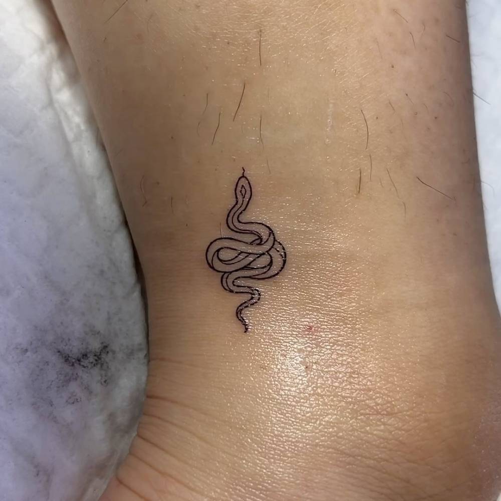 Fine line style snake tattoo placed on the ankle.
