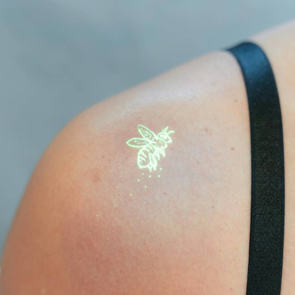 Illustrative style UV ink bee tattoo located on the shoulder.
