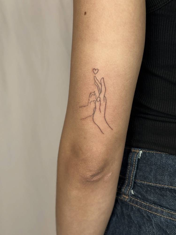 Dog high five tattoo located on the tricep, fine line style.