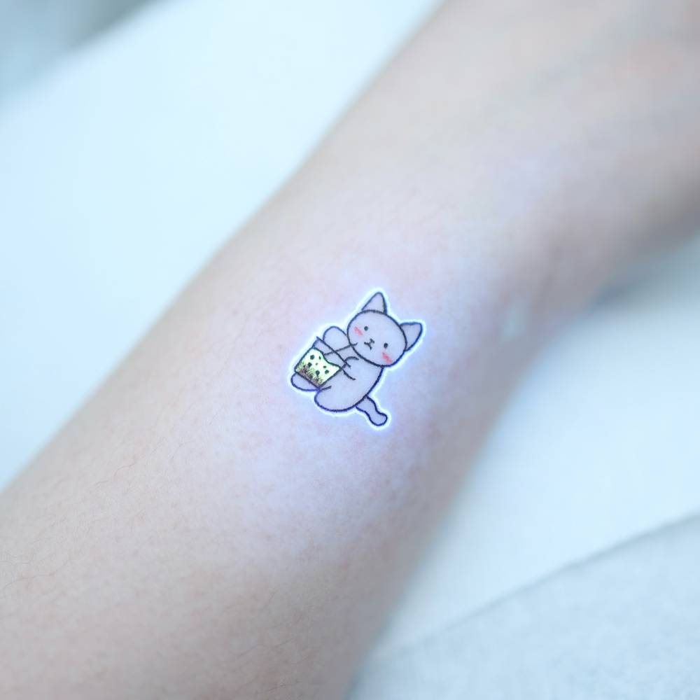 Cartoon style cat tattoo in UV ink located on the wrist.