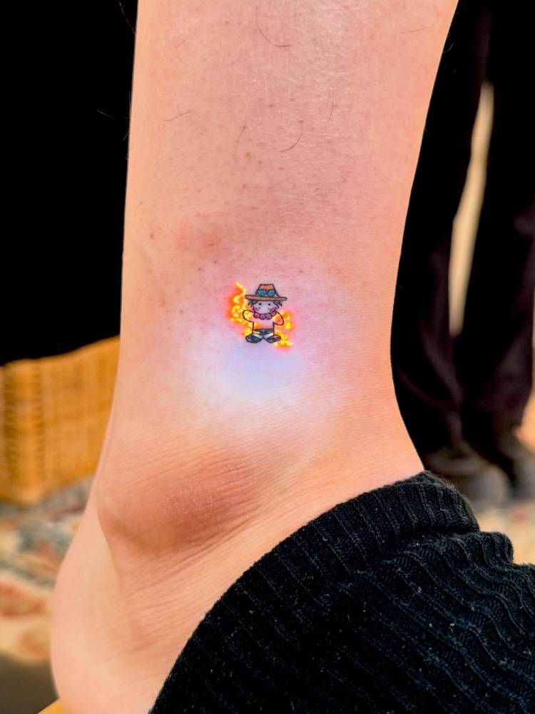 Ace from 'One Piece' tattooed on the ankle, cartoon style.