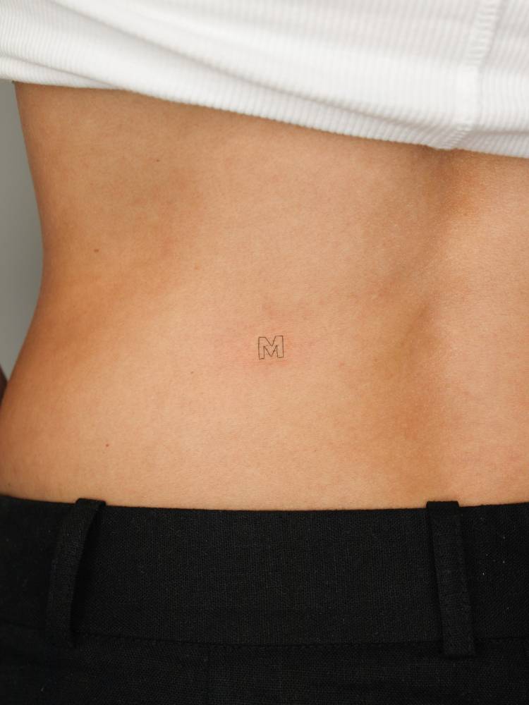Tiny letter "M" tattoo located on the lower back.