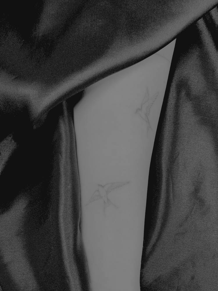 Flying swallows tattooed on the upper arm, fine line style.