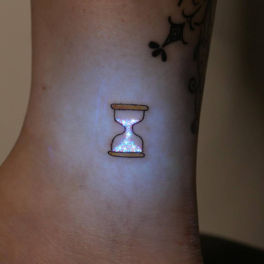 Little hourglass tattoo in illustrative style placed on the ankle.