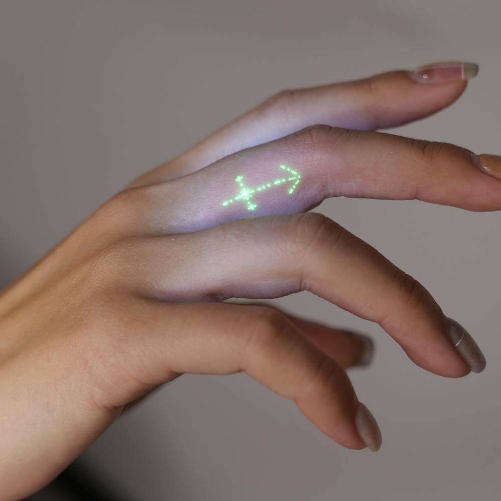 Sagittarius symbol tattoo in UV ink placed on the finger.