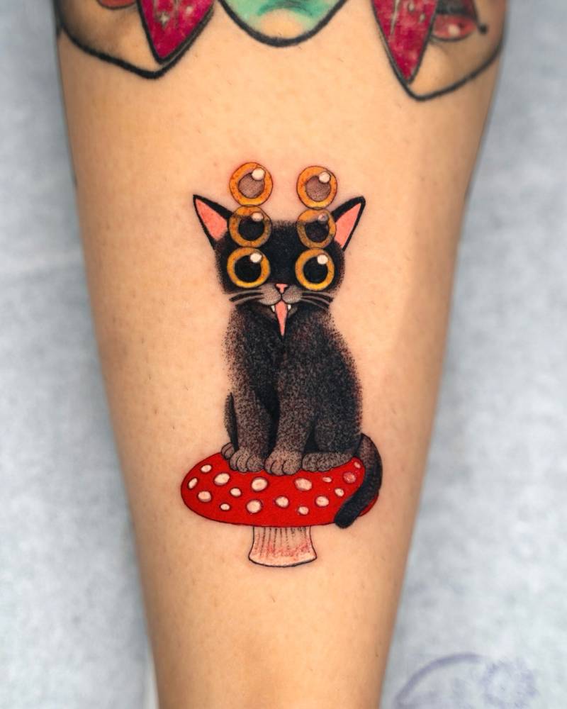 Cartoon style black cat and mushroom tattoo located on the achilles.