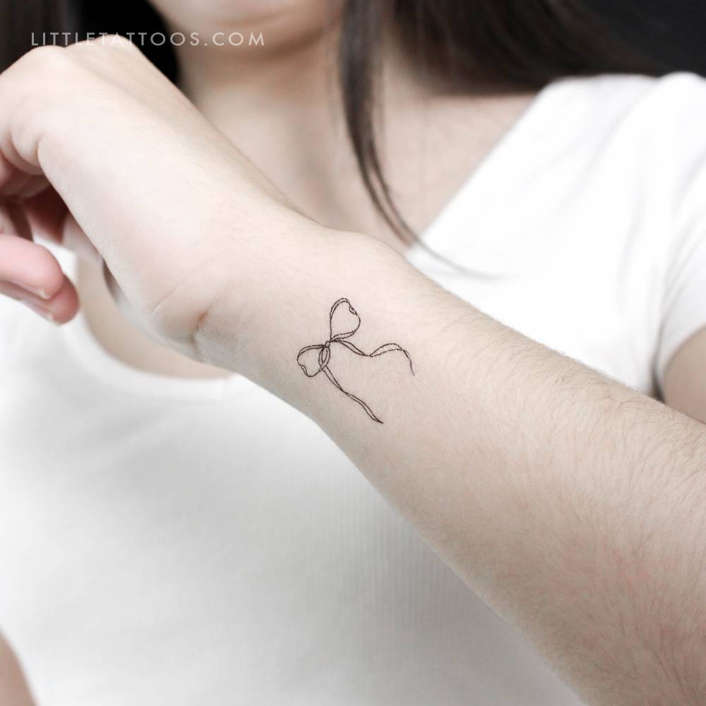Fine line style ribbon bow temporary tattoo located on the wrist.