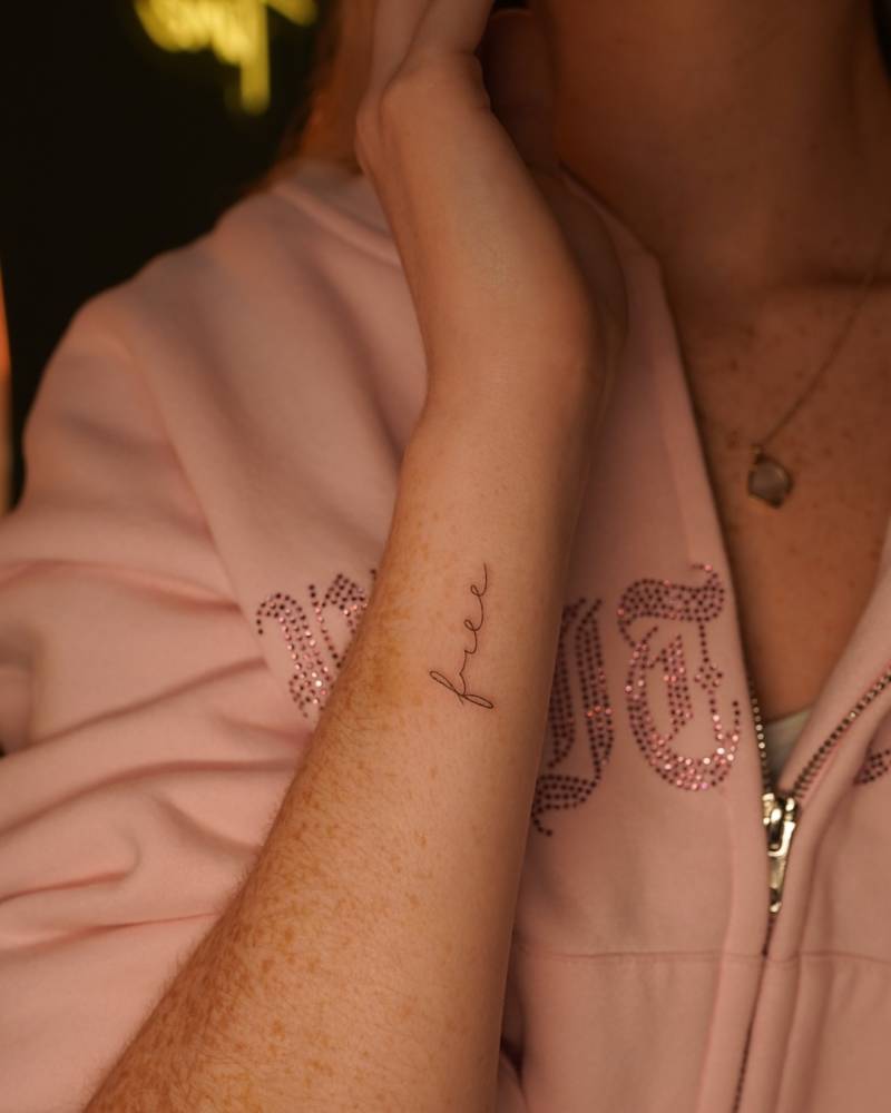 Handwritten font word "free" tattoo located on the wrist.