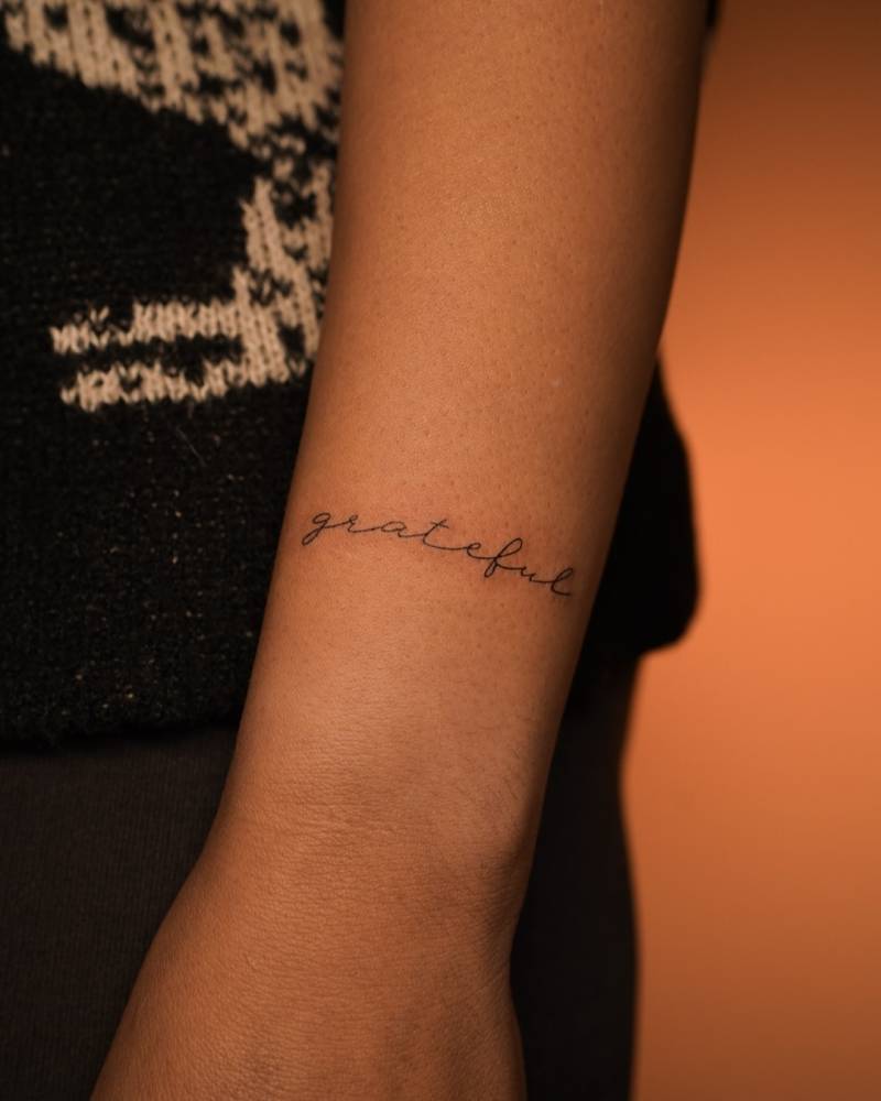 Word "grateful" lettering tattoo done on the wrist.