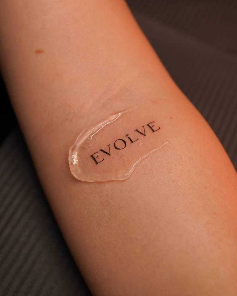 Word "evolve" in serif font tattooed on the inner forearm.