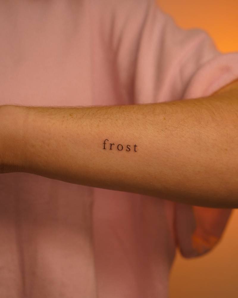 Word "frost" in serif font tattooed on the wrist.