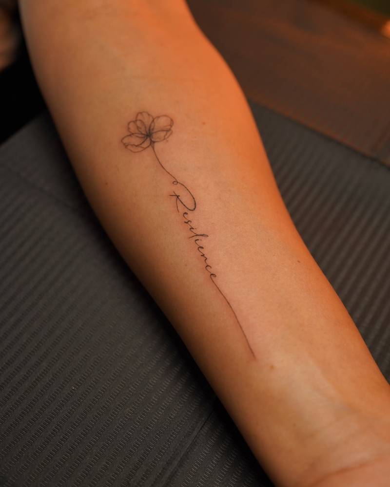 Flower and word "resilience" tattooed on the inner forearm.