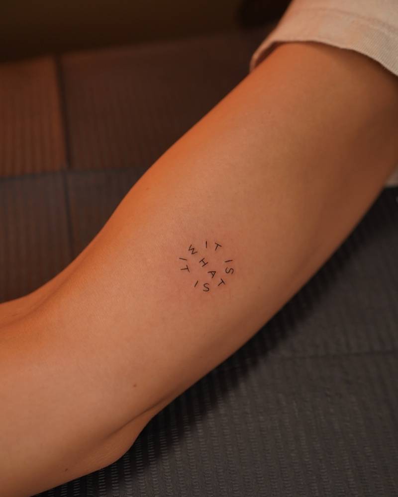 "It is what it is" lettering tattoo placed on the inner arm.