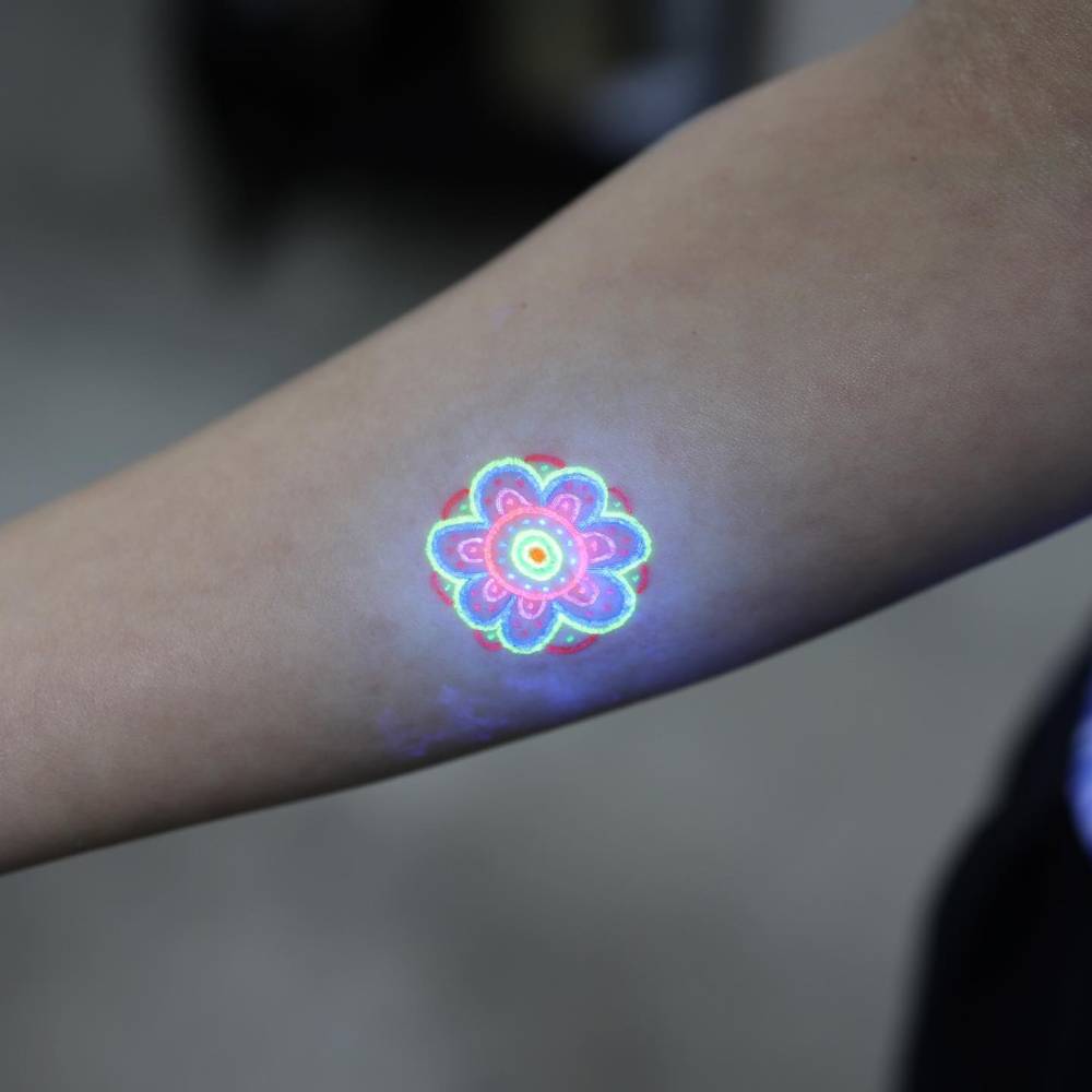 UV ink flower tattoo in illustrative style placed on the inner forearm.