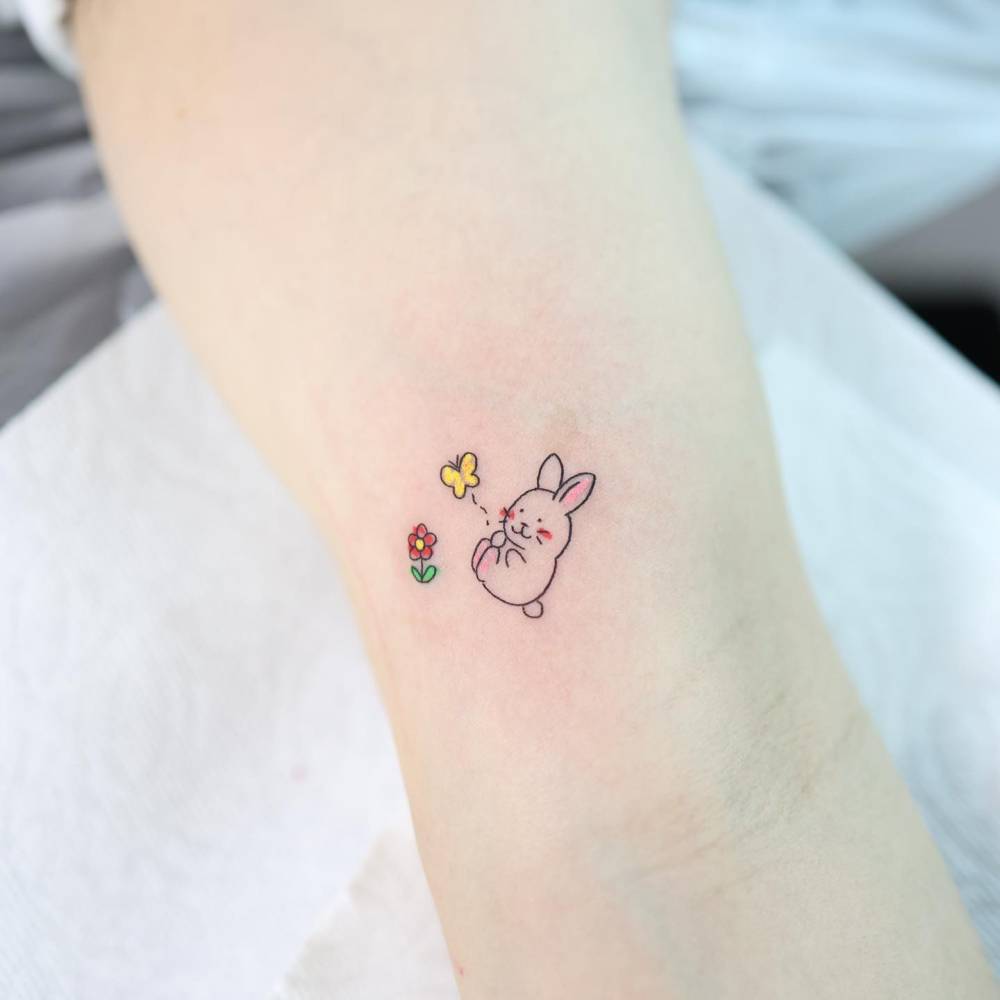 Cute little rabbit tattoo located on the inner arm, cartoon style.