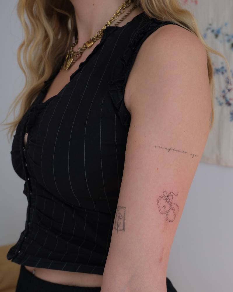 Fine line style heart pendant tattoo located on the upper arm.