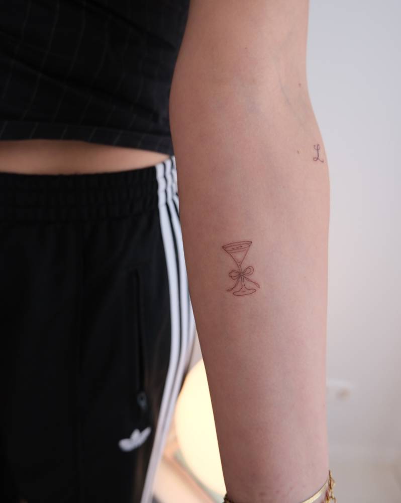 Fine line style cocktail tattoo located on the inner forearm.