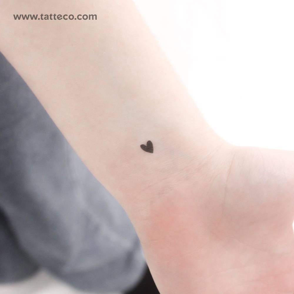 Tiny minimalistic black heart temporary tattoo located on the wrist.