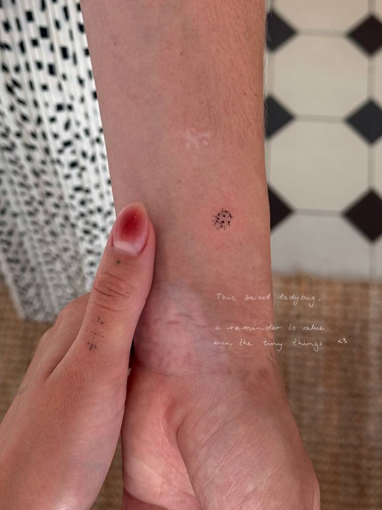 Tiny ladybug tattoo in illustrative style located on the wrist.