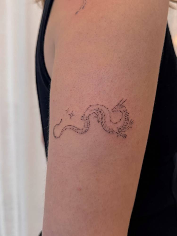 Dragon tattoo in fine line style located on the upper arm.