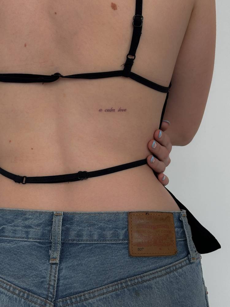 "A calm love" lettering tattoo placed on the back.