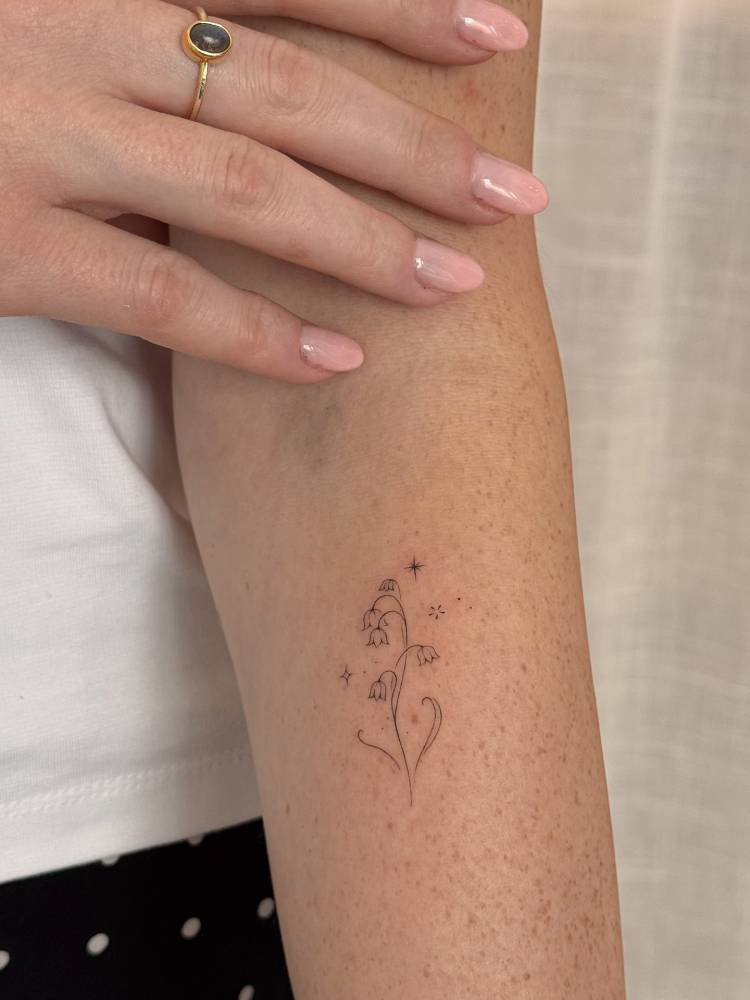 Lily of the valley flowers tattooed on the forearm, fine line style.