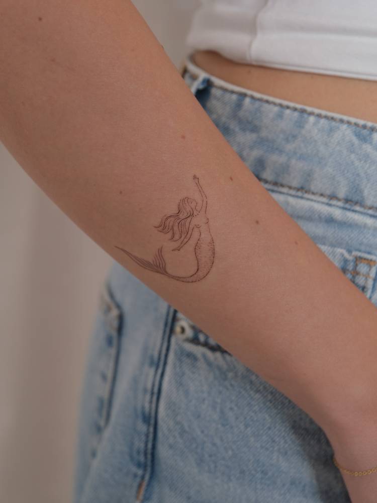 Cute mermaid tattoo in fine line style done on the forearm.