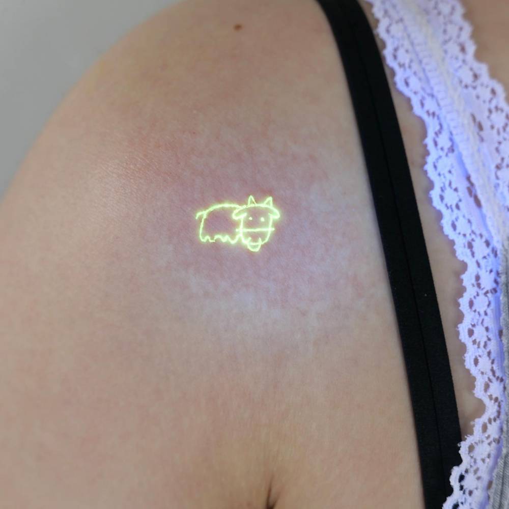 Ignorant style cow tattoo in UV ink placed on the shoulder.