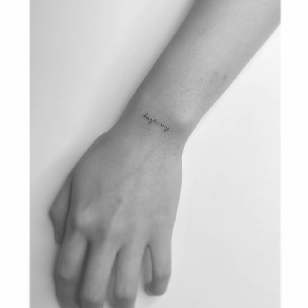 Handwritten font name tattooed on the wrist.
